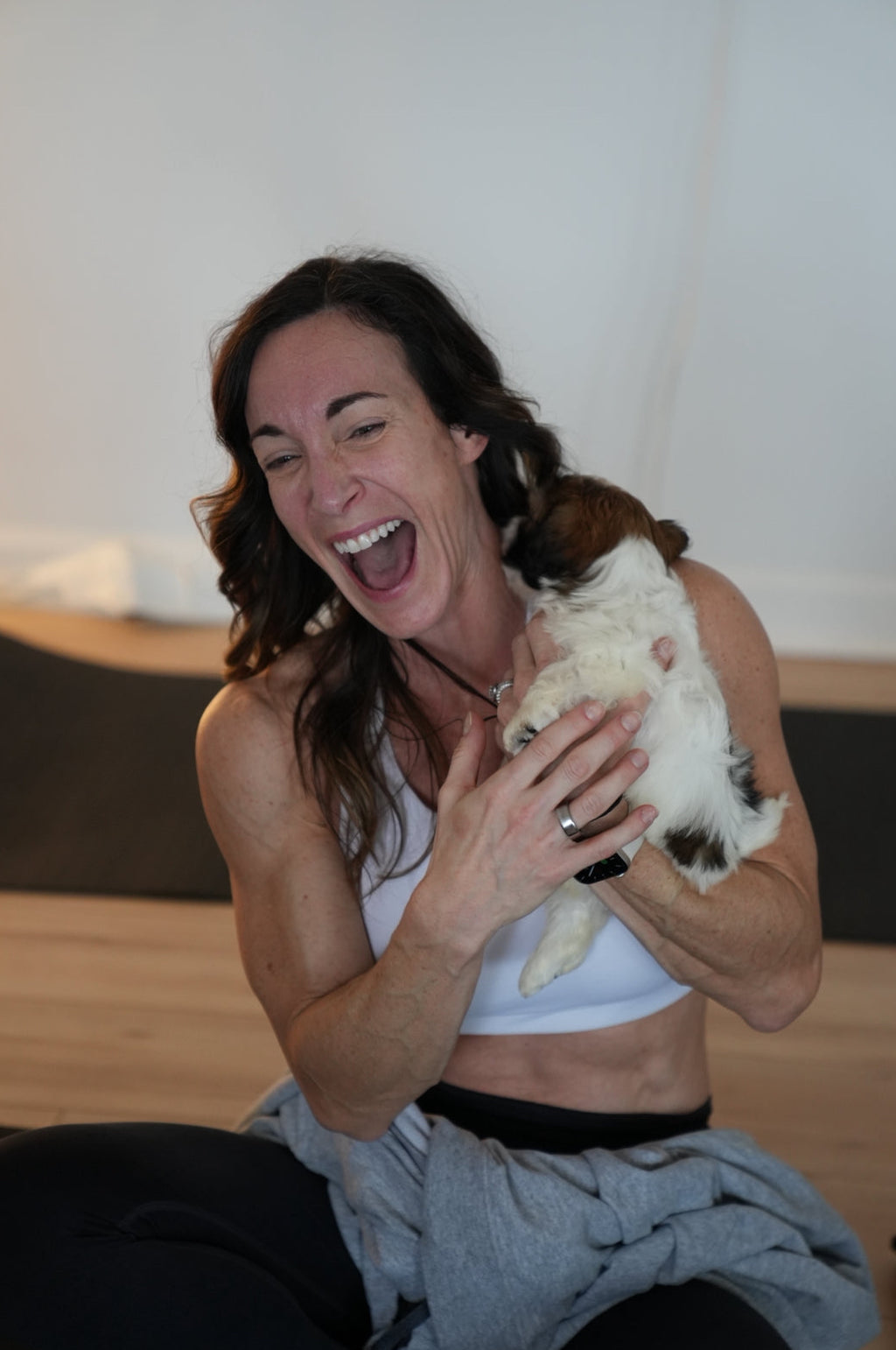 Woman laughing joyfully while holding a small dog indoors during puppy yoga class by Reset Vibes in Chicago suburbs