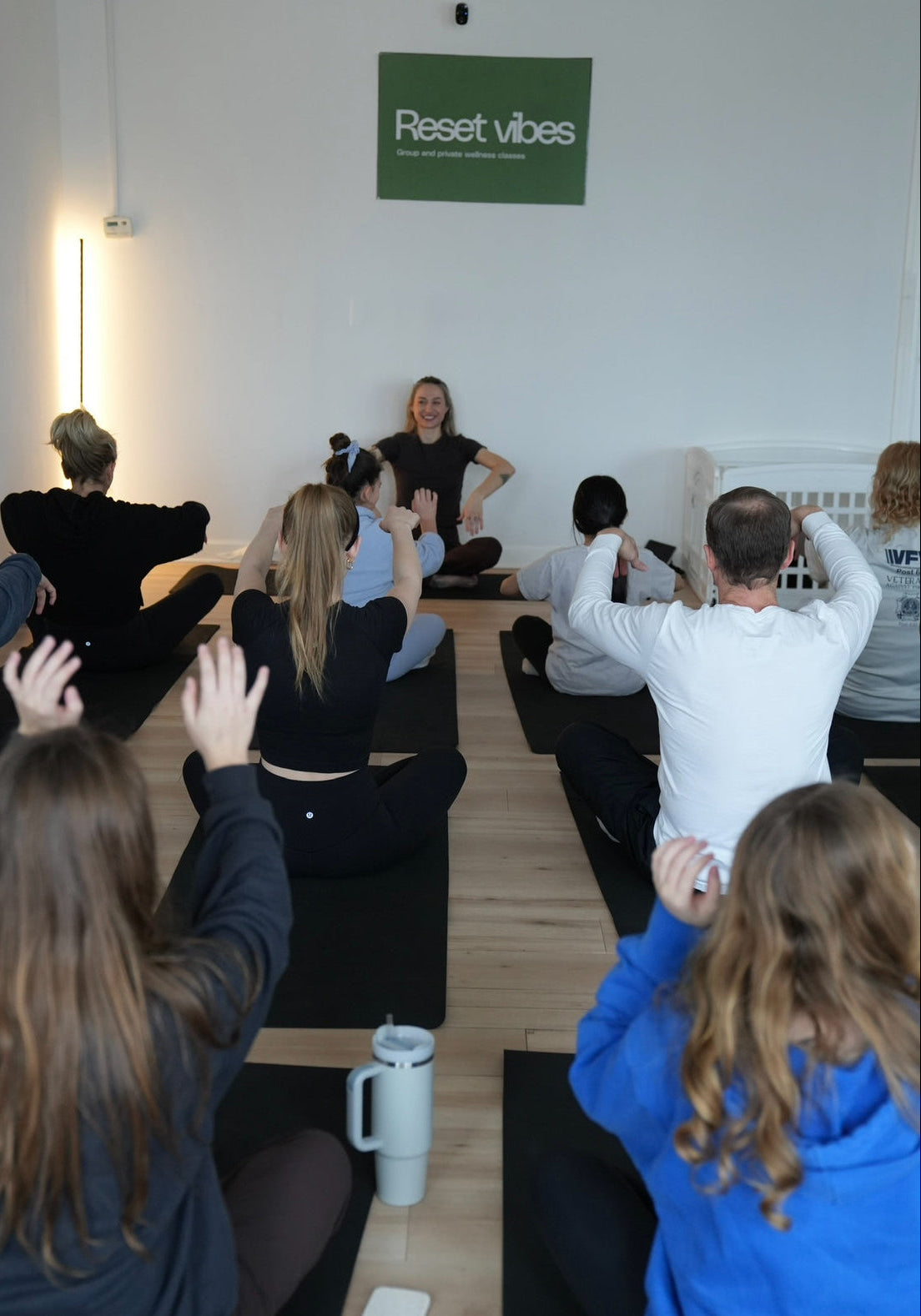 Group of people participating in a yoga or meditation session with 'Reset vibes' sign in the background.