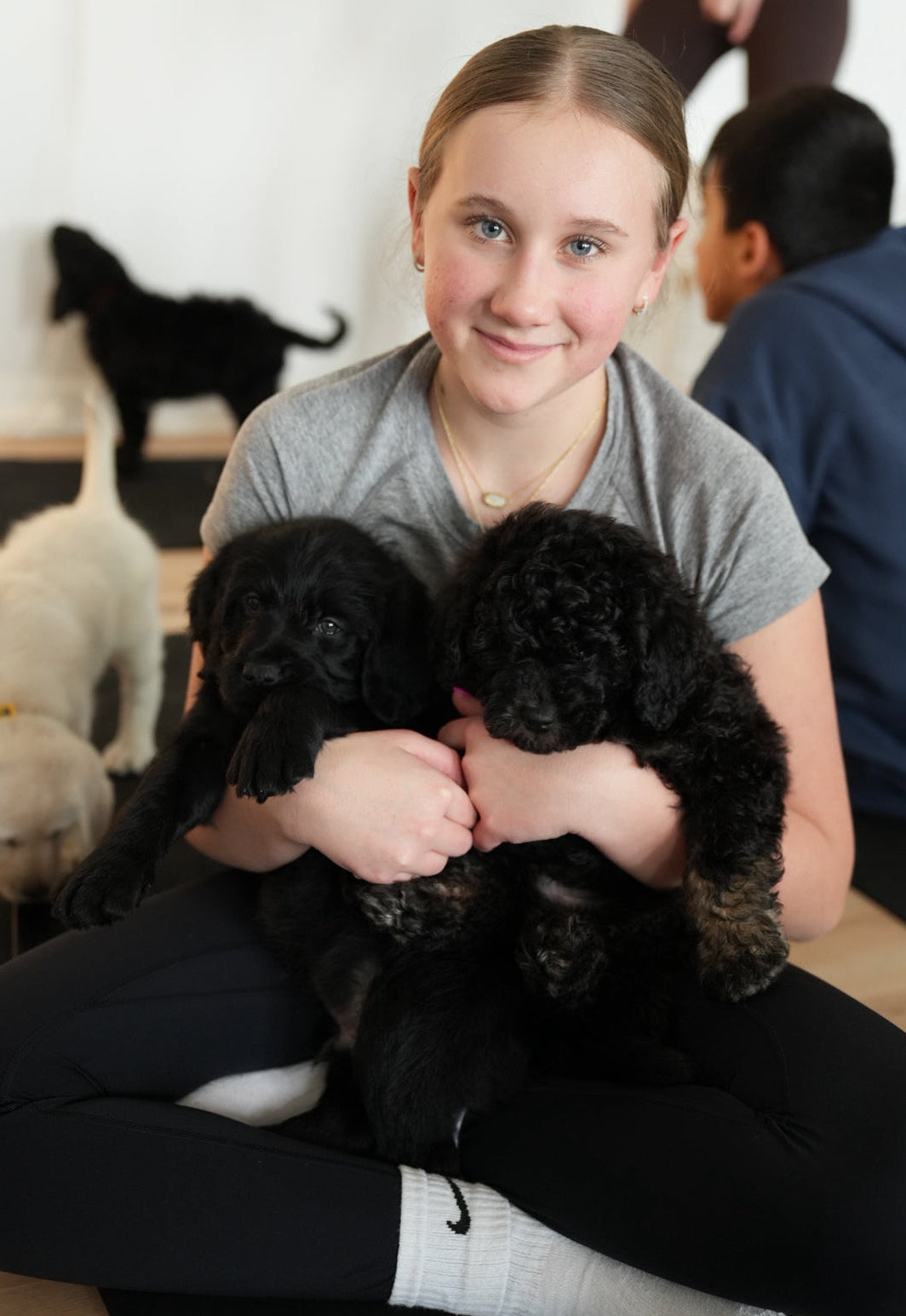 Young girl holding two black puppies with a neutral background During puppy yoga class at Reset Vibes Chicago